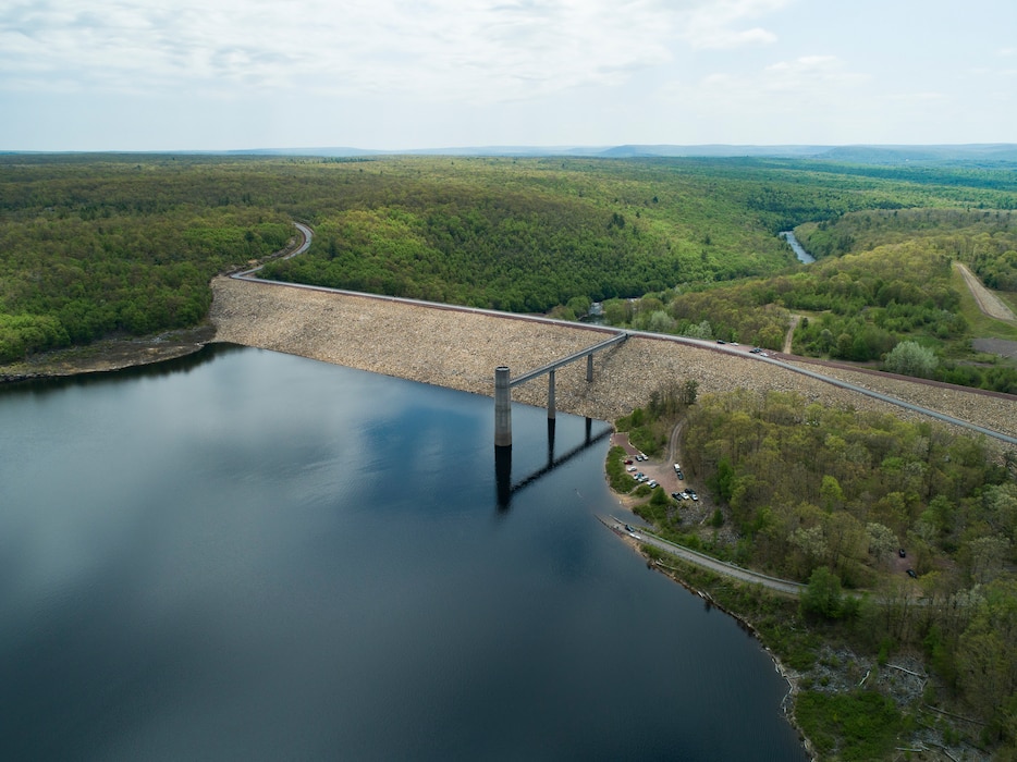 An aerial view of the Francis E. Walter Dam. Water is pooled in the left of the image and the dam runs through the image's center. A forested area appears in the image's right side.