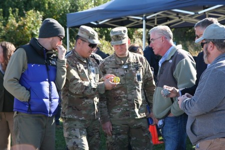 Attendees examine a commercial-off-the-shelf chemical sensing puck alongside the WILE-E 3.0 Modular Deployable CBRN Microsensor Concept Puck used during a Deployable CBRN Microsensor Integration Experiment at Aberdeen Proving Ground.
