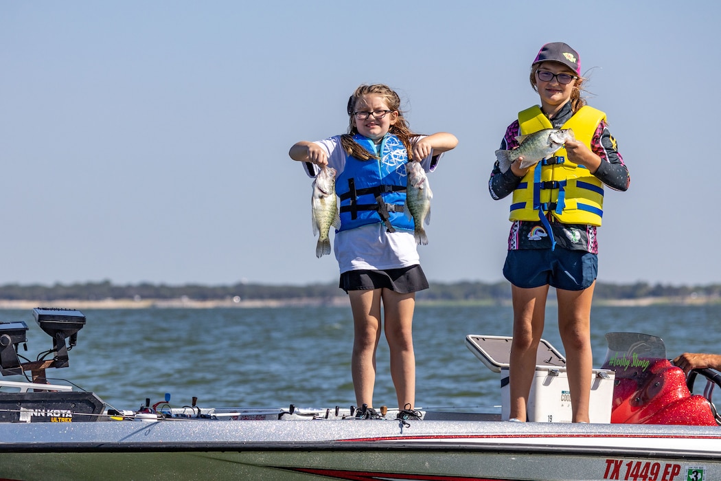 children on a boat on a lake pose for a photo while holding fish