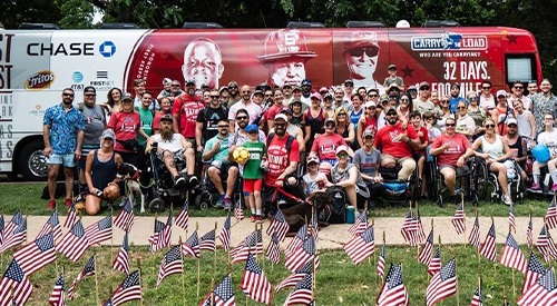 Carry The Load participants honor and remember Veterans at a national cemetery behind a field of American flags they placed at headstones and markers during Memorial May.