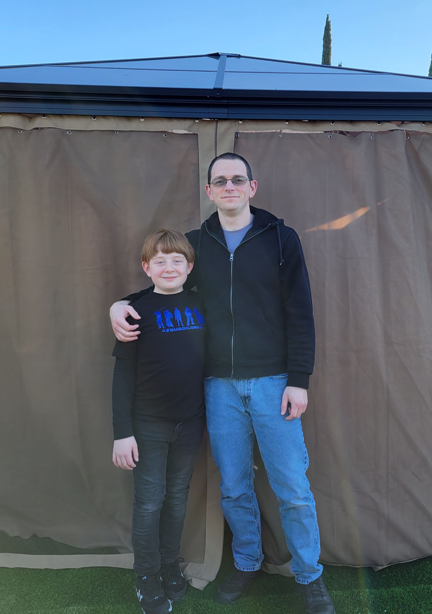 A man and his son pose for a photo in front of a gazebo.