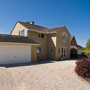 gravel driveway leading up to house and garage with stone siding and blue sky in background