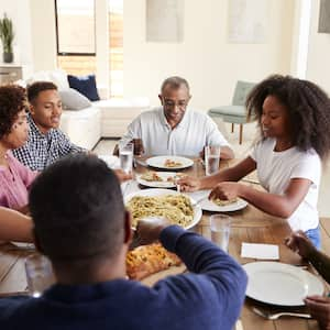 Three generation Black family eating dinner together at wood dining room table 