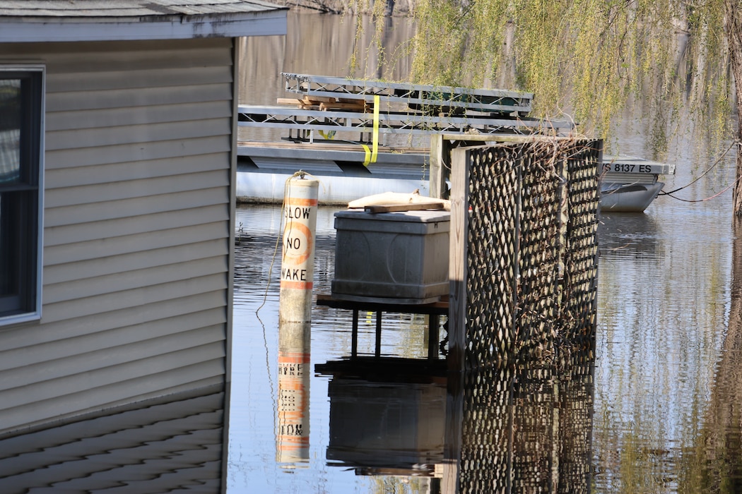 Water is high next to fence, house, buoy sign, clear, sunny day