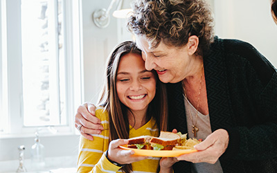 Older woman hugging girl and handing her a lunch plate