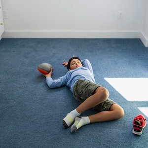 Boy holding a ball lying on carpet in his bedroom