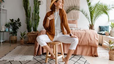 A fashionable young woman sitting on a wooden stool in front of her bed with a macrame headboard