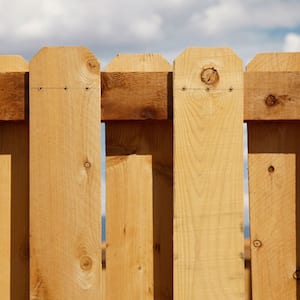 A cedar board-on-board picket fence and a cloudy blue sky