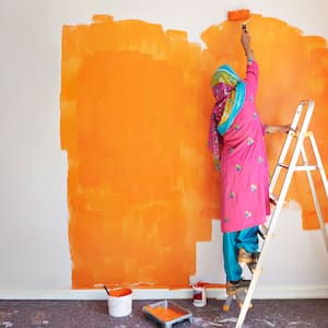 A woman on a ladder painting a room with a paint roller