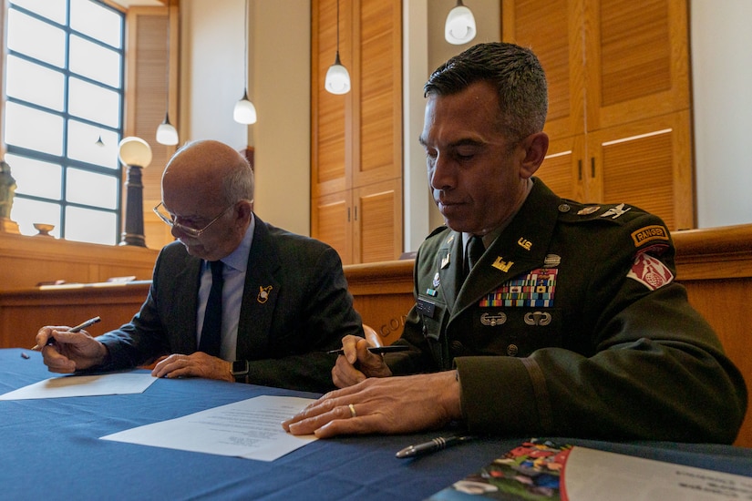 Two men sitting at a table signing papers.