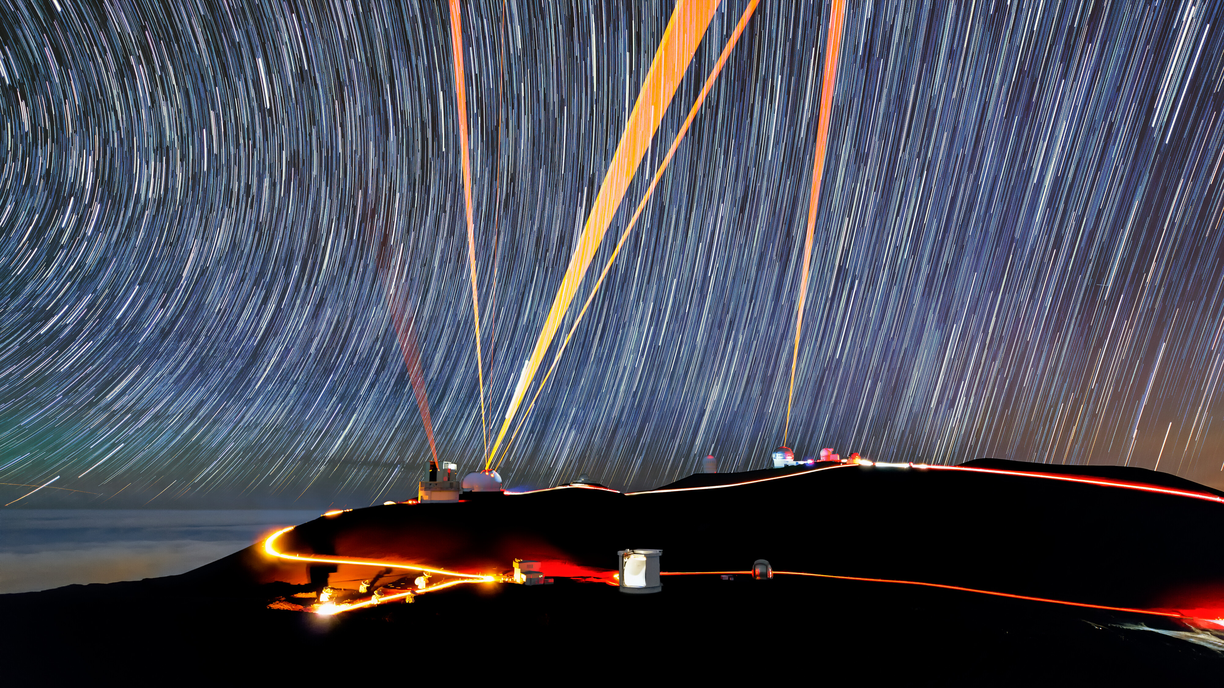 Star trails blur and lasers streak across the sky in this long-exposure view from Pu‘u Poli‘ahu, the mountain peak adjacent to the GeminiObs North telescope.
Gemini North can be seen slightly to the right of the center of this image, shooting its laser into the sky. A handful of other telescopes that are part of the Maunakea Observatories in Hawai‘i surround Gemini North.