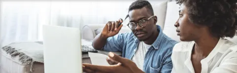 Worried couple looking at bills online using laptop.