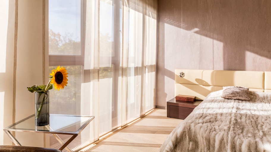 A sunlit bedroom with a sunflower in a vase