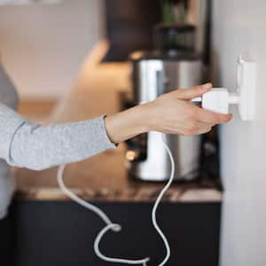 shot of woman in gray shirt plugging in power cord of coffee pot to electrical outlet