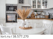 Still-life. Dried pampas grass in a vase, white ceramic pumpkins, a teapot and pumpkin-shaped candles on a white table in the interior of a Scandinavian-style home kitchen. Cozy autumn concept. Стоковое фото, фотограф Photojuli / Фотобанк Лори