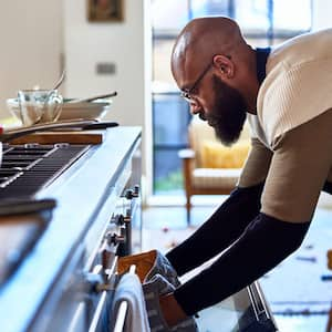 A man is cooking dinner by placing a pan into the oven