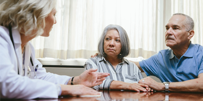 An older couple, holding hands, talking with a doctor