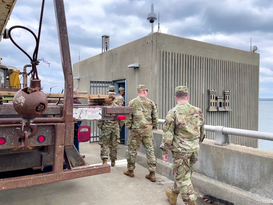 Three soldiers in uniform walk across a dam.