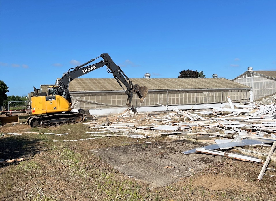 Excavator demolishing an old screenhouse on a research farm.