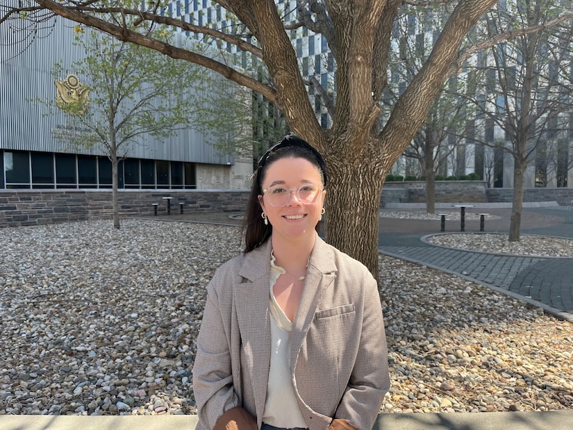 A woman sits on a bench in front of tree and smiles.