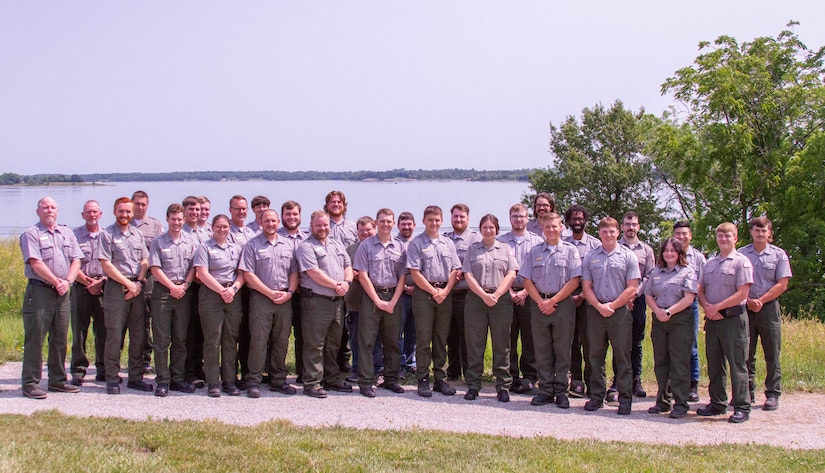 Several uniformed park rangers stand and pose for a photo in front Smithville Lake with trees and the lake in the background.