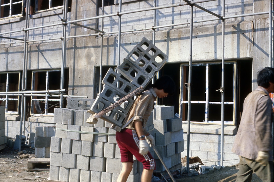 Men carries large blocks on his back.