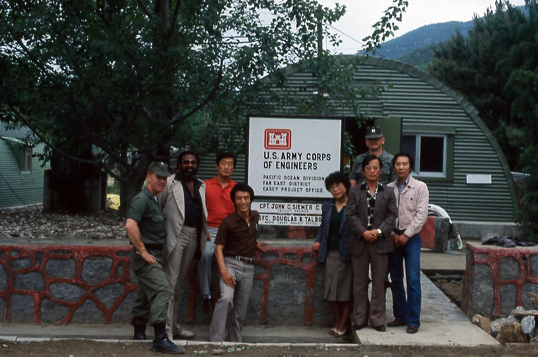 Eight men and women stand outside near a sign.