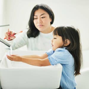 Mother helping daughter to wash her hands in the bathroom