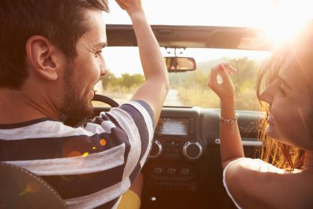 Young couple driving along country road in open top car.