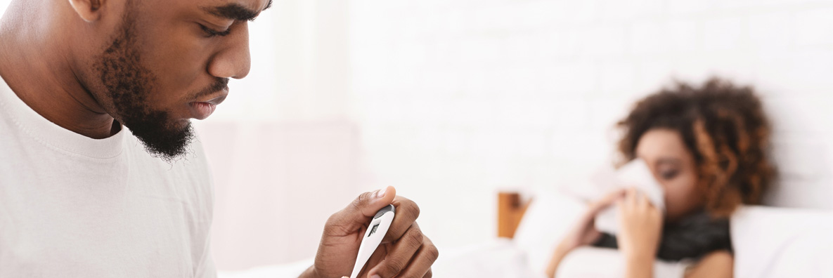 sick woman in bed man checking temperature on thermometer