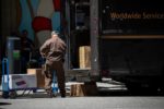 A UPS DRIVER HANDLES A HAND CART OUTSIDE A UPS TRUCK