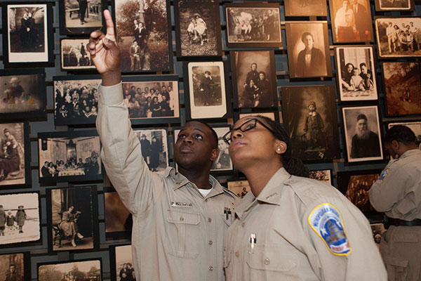 Two uniformed Museum visitors point up to a photo in the Tower of Faces