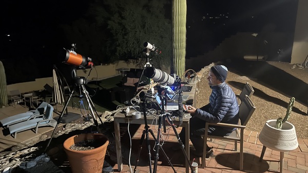 Man sitting at a table outside controlling a set of three telescopes.