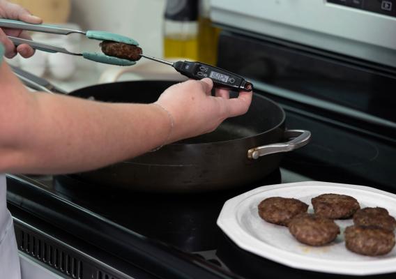 A person inserting a food thermometer into sausage