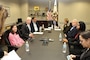 People wearing business attire sit at a large conference room table.