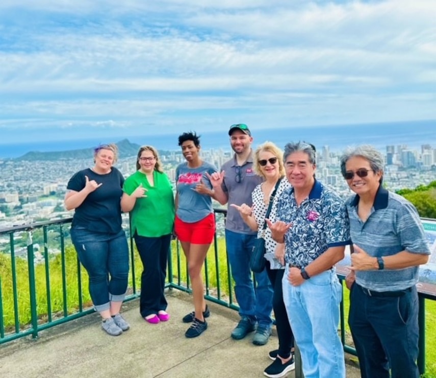 A diverse group of people stand on an overlook with the city of Honolulu Hawaii in the background.