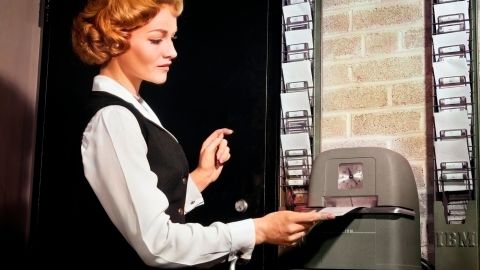 1960s Woman Punching Time Clock At Work. (Photo by Debrocke/Classicstock/Getty Images)