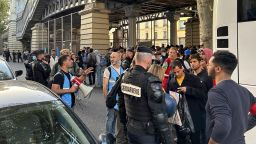 Migrants board a bus that will take them away from Paris as police stand guard