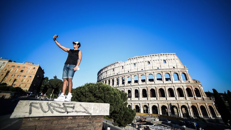 A young man takes a selfie photo by the Colosseum monument in Rome on May 21, 2020.