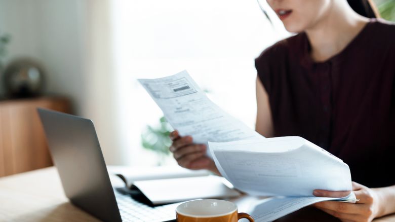 Cropped shot of Asian woman sitting at dining table, handling personal finance with laptop. She is making financial plan and planning budget as she go through her financial bills, tax and expenses at home. Wealth management, banking and finance concept