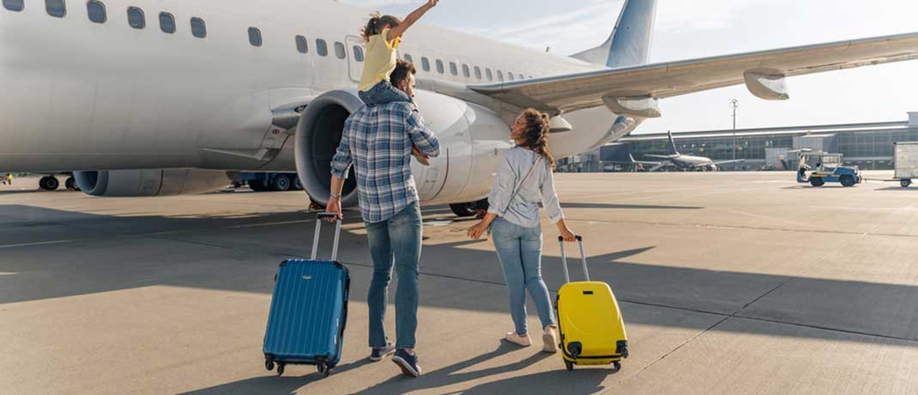 Young family walking with suitcases toward an airplane