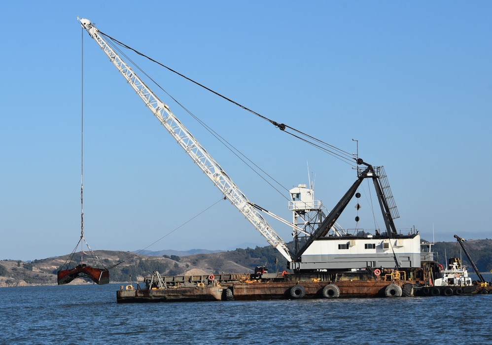 A white dredge on blue water with hills in the background