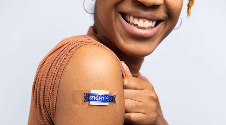 Woman smiling showing her arm where she has a band-aid that says “Fight Flu”