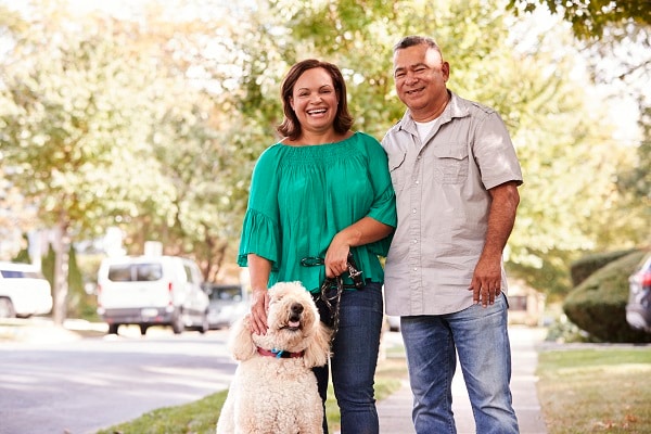 Portrait Of Senior Couple Walking Dog Along Suburban Street