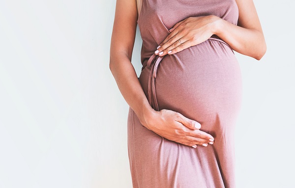 Pregnant woman in dress holds hands on belly on a white background.