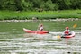 Two park ranges kayak through a gorge with paddles in motion as they push to go downstream.