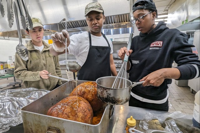 Spc. Shaheed Henry, a culinary specialist with 2nd Brigade Combat Team, pours glaze over the ham as Soldiers work through the night to prepare a Thanksgiving feast for 10th Mountain Division (LI) Soldiers and family members Nov. 21 at the Commando Warrior Restaurant. 