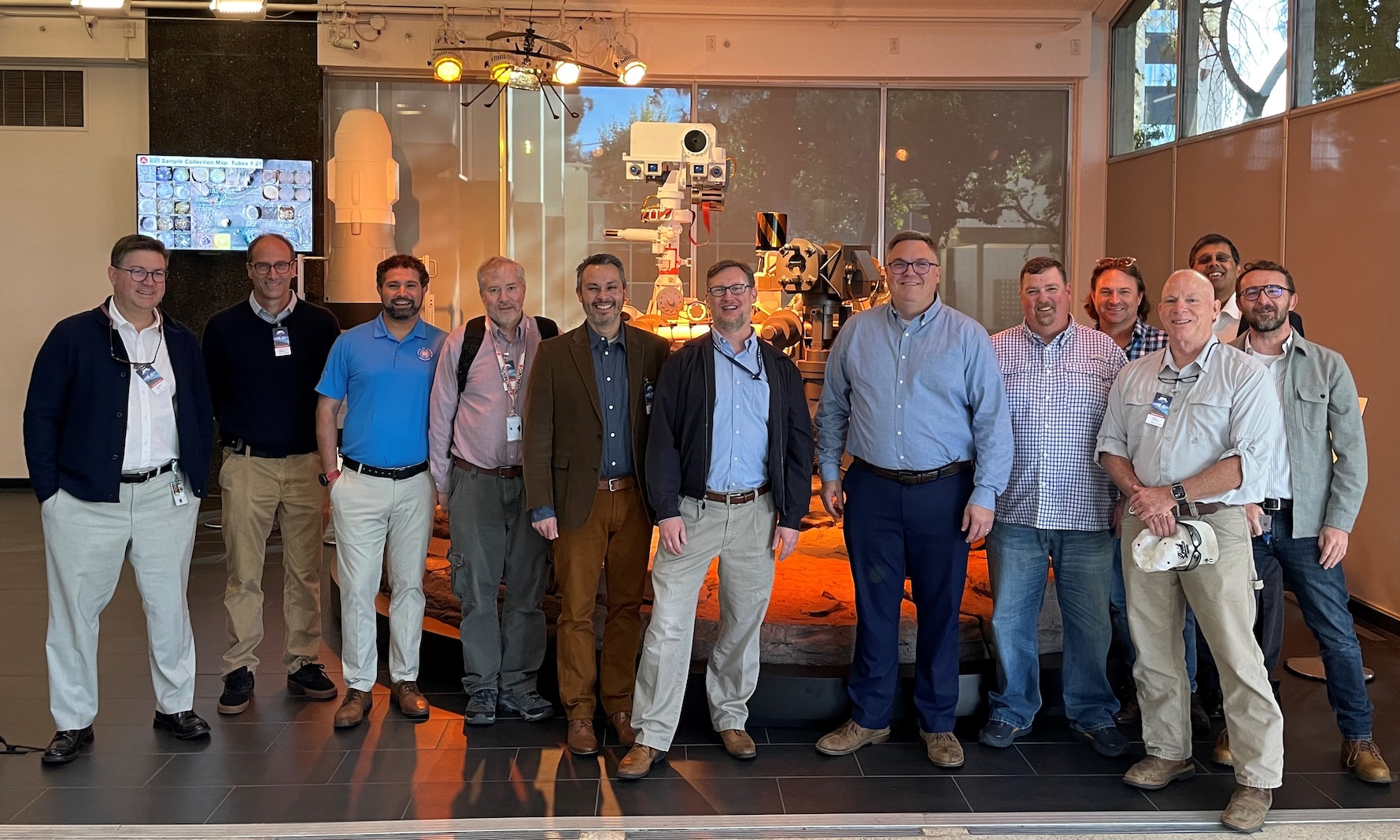 Group of men standing beside each other in front of NASA space equipment.