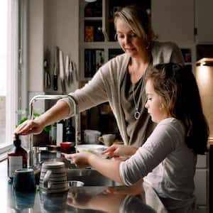 Daughter washing dishes while standing by mother in the kitchen