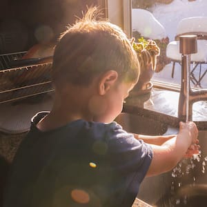 Little boy washes hands at kitchen sink, winter scene thru windows